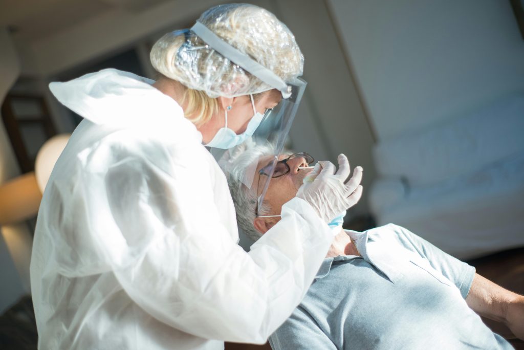 Healthcare worker in protective gear performing a COVID-19 test on a patient indoors.
